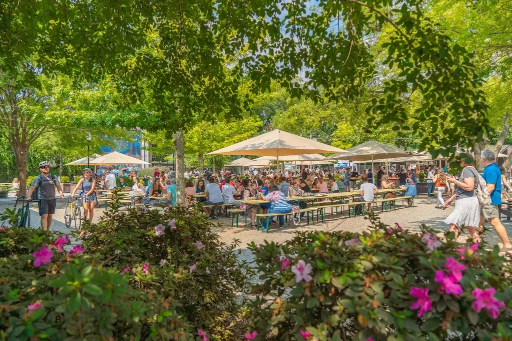 Outdoor patio with people, picnic tables, large umbrellas, and trees.