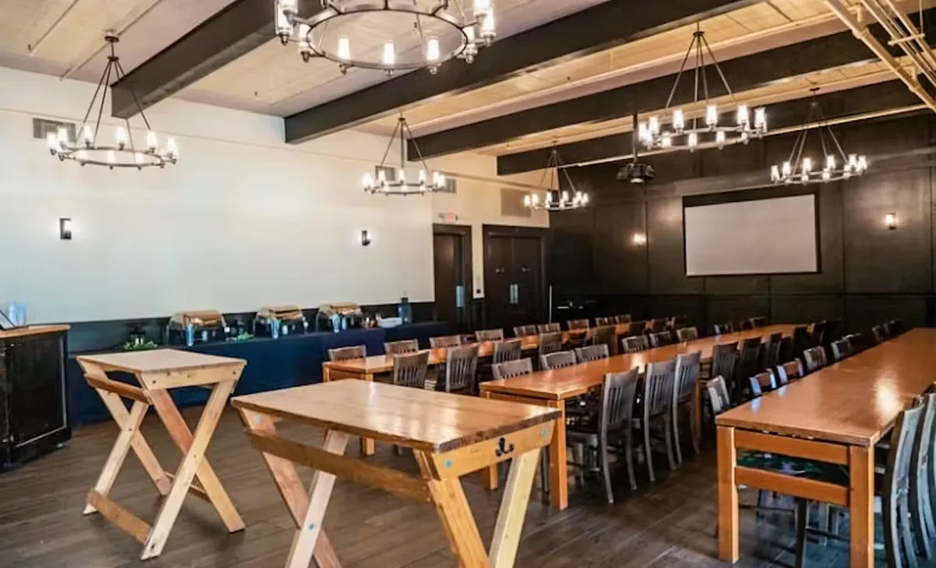 Spacious, empty banquet room with wooden tables, buffet, projector screen.