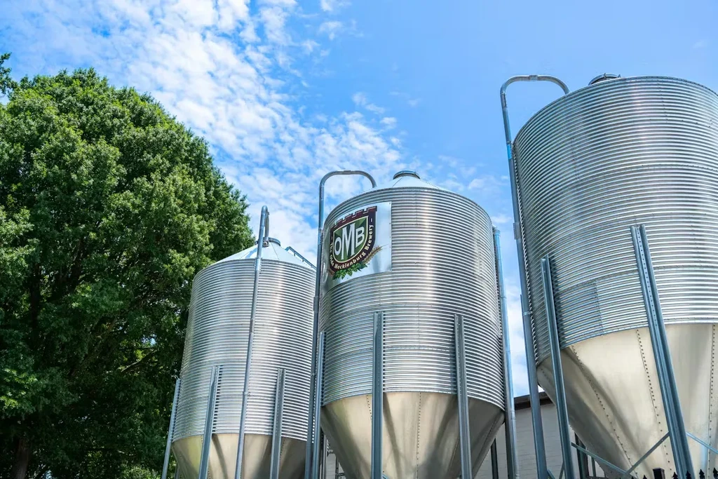 Olde Mecklenburg Brewery's three corrugated silos outdoors with a tree.