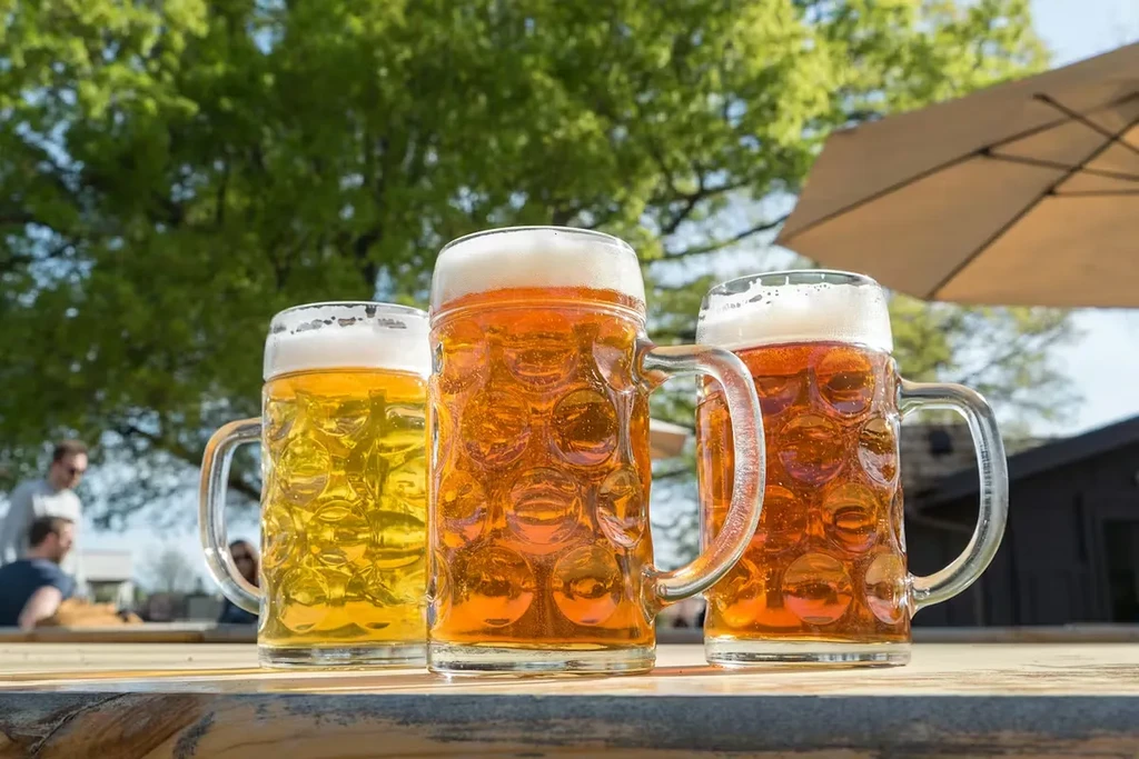 Three steins of amber and yellow beer on an outdoor rustic table.