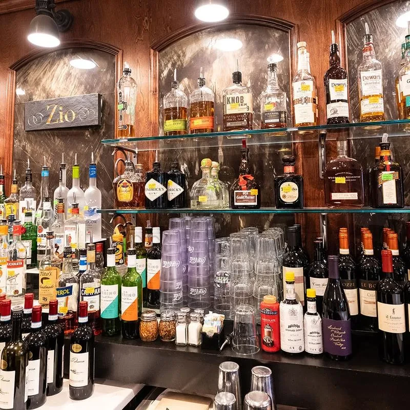 Illuminated bar area filled with liquor bottles and a gold "Zio" sign.