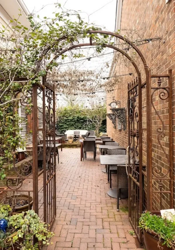 Rustic iron archway entrance to an outdoor brick patio with seating.