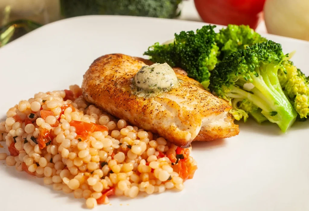 Close-up of pan-seared chicken, melting butter, couscous, and broccoli.