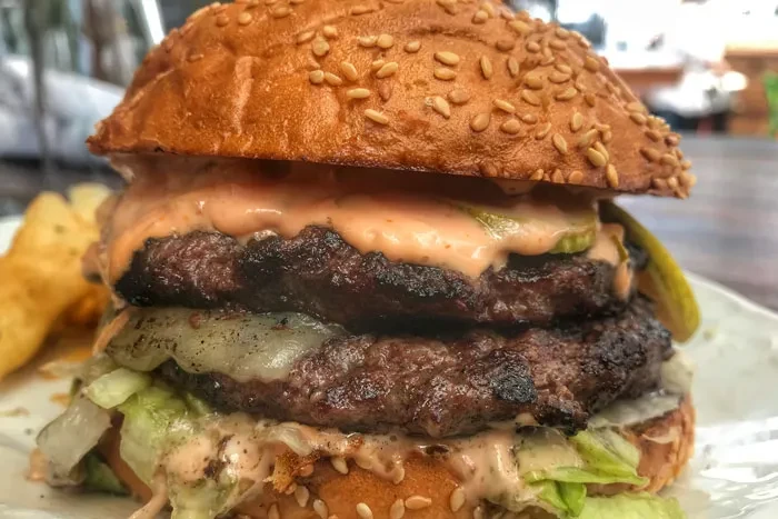 Close-up char-grilled double cheeseburger with melted cheese, lettuce, pickles, and sauce.