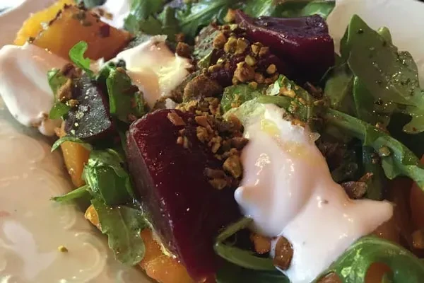 Close-up of a plated salad with beets, greens, creamy cheese, and pistachios.