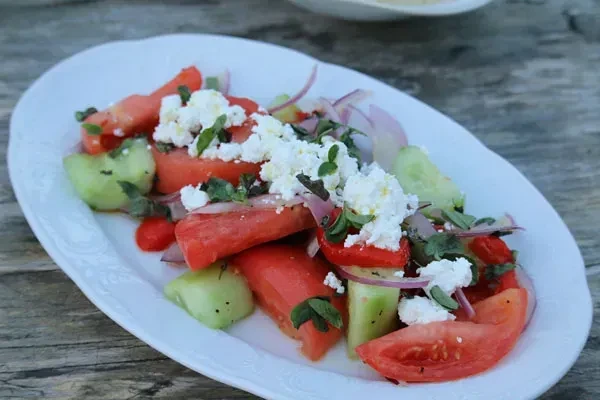 Fresh tomato, cucumber, onion, feta salad on a wooden table.
