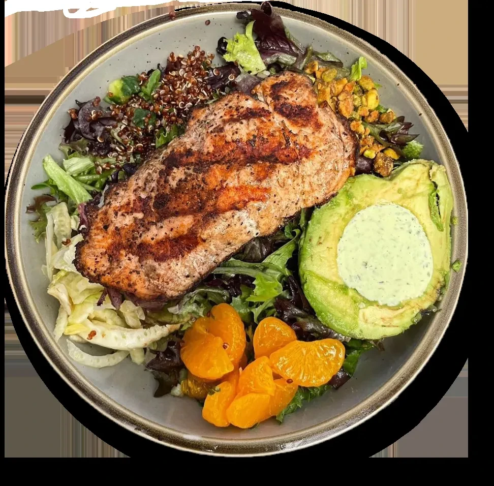 Overhead view of a bowl with grilled fish, greens, avocado, quinoa, citrus.