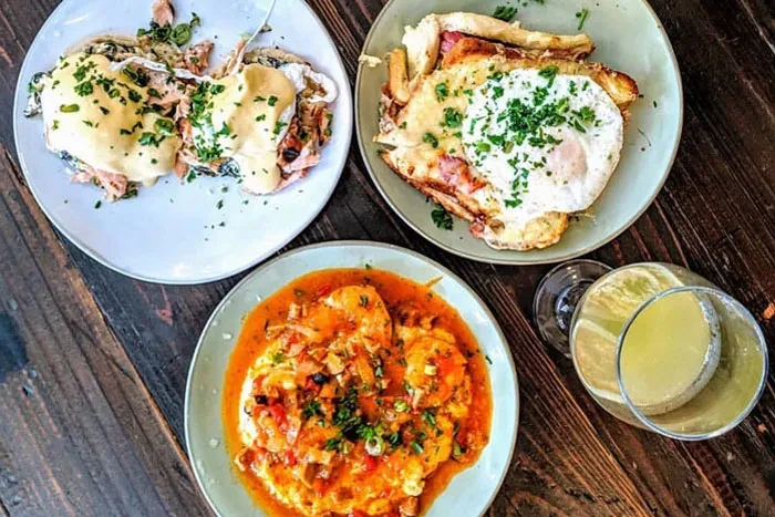 Overhead view of Eggs Benedict, cheesy toast, shrimp stew, and a drink.