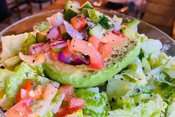 Close-up of vibrant salad with avocado, tomatoes, onions, and lettuce.