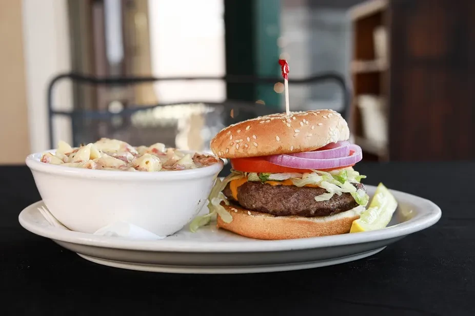 A burger, pickle spear, and creamy salad on a white plate.