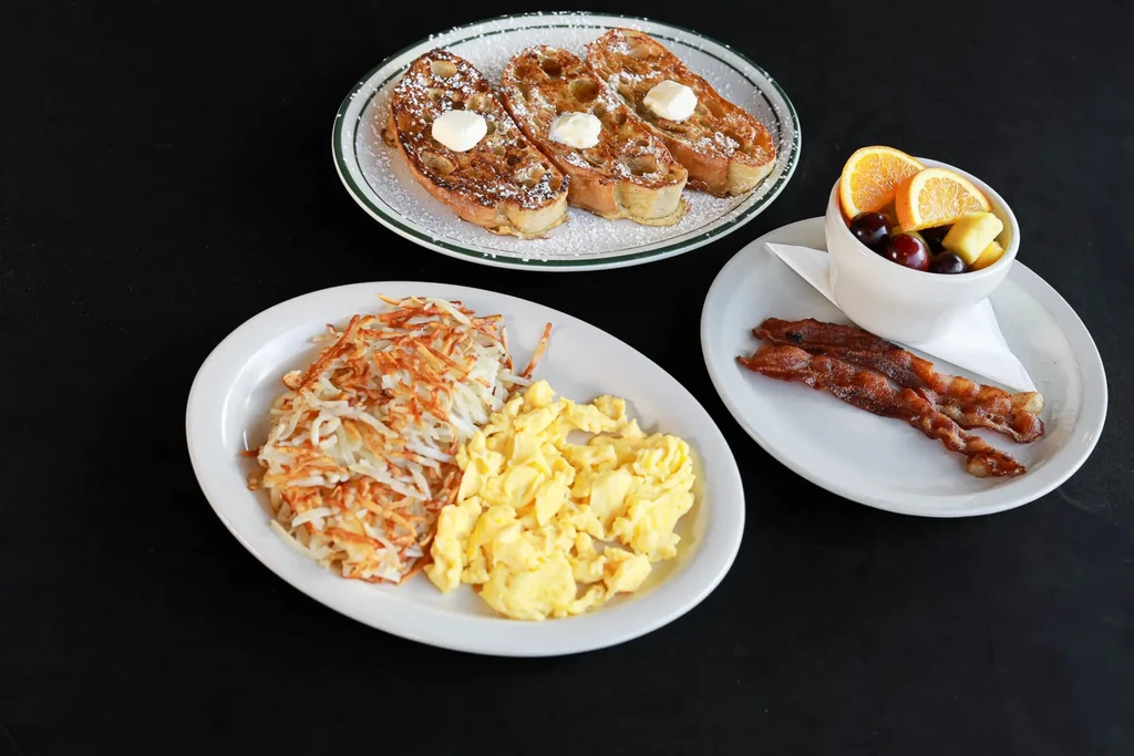 Breakfast plates feature French toast, scrambled eggs, bacon, hash browns, and fruit.