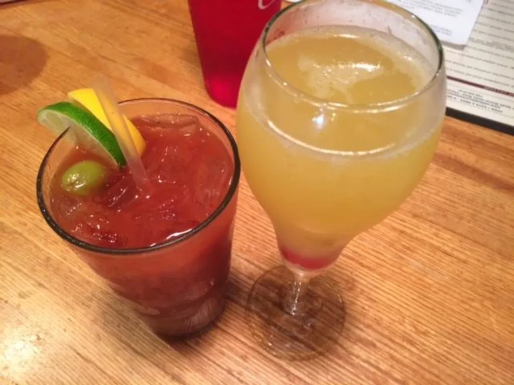 A garnished Bloody Mary and a Mimosa on a rustic wooden table.