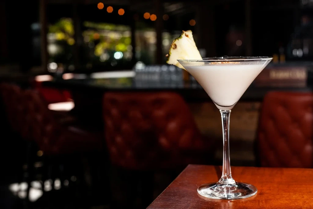 Creamy white cocktail with pineapple slice and spice in a martini glass.