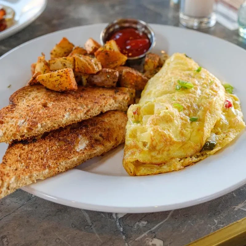 Breakfast plate: omelet, seasoned potatoes, toast, and ketchup ramekin.