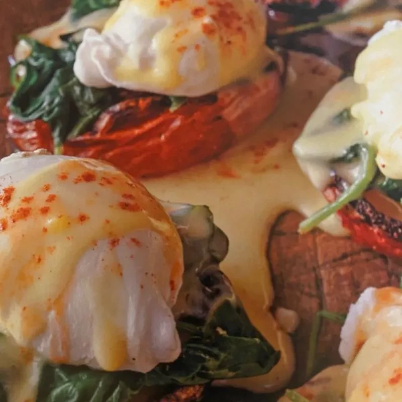 Eggs Benedict with hollandaise, spinach, and roasted vegetables on a rustic surface.