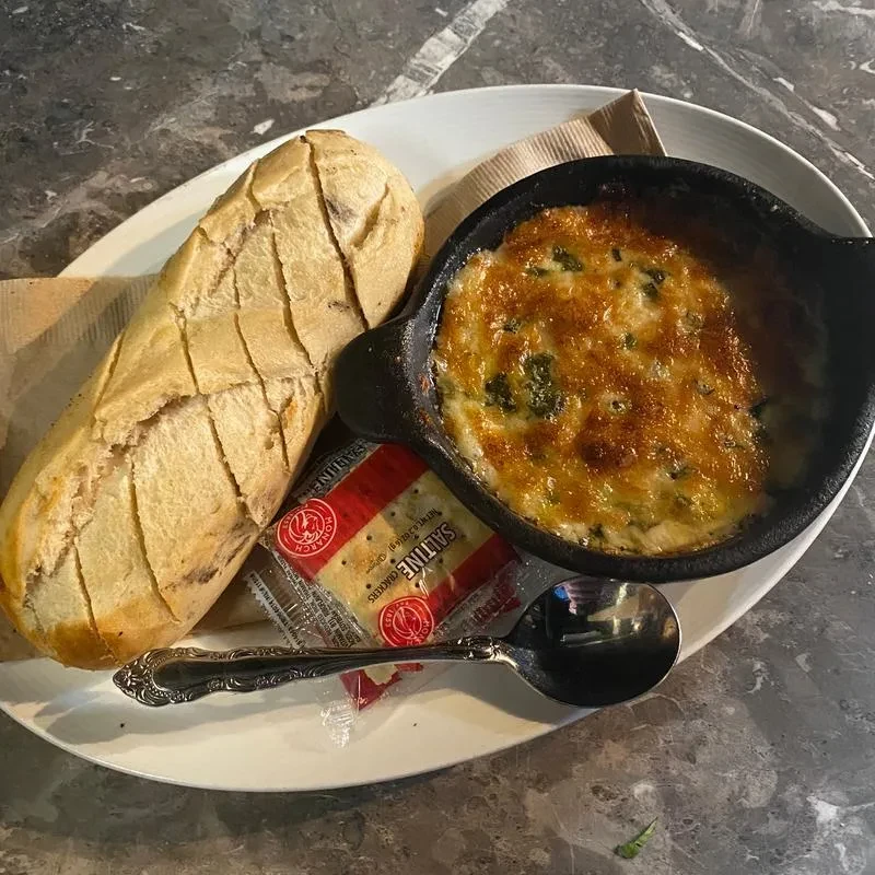 Baguette, bubbling gratin dip, and crackers on a dark table.