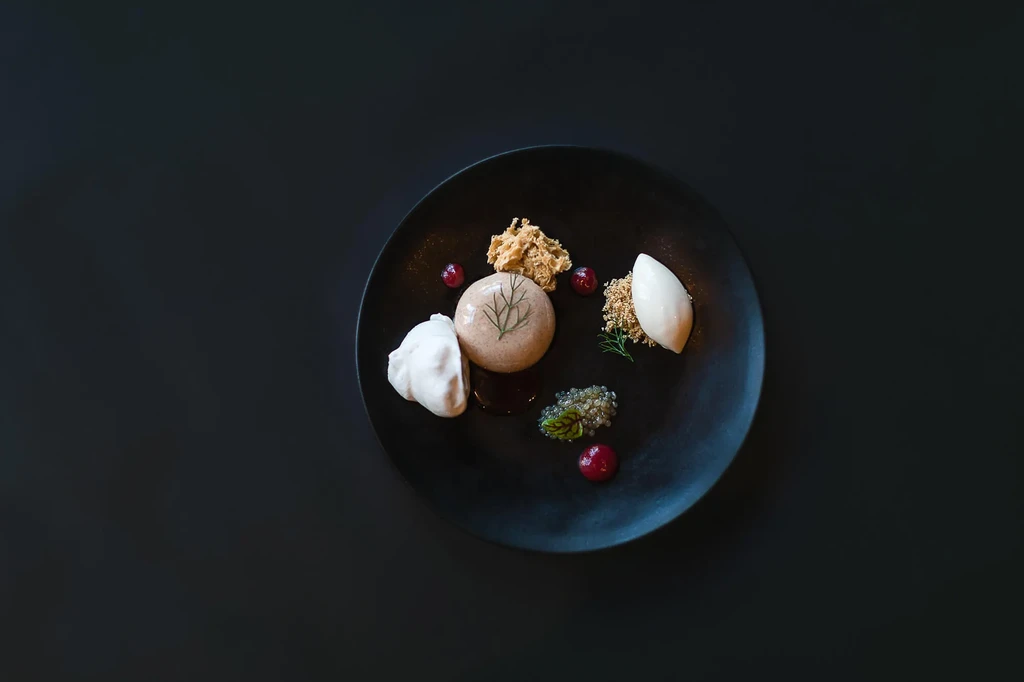 Meticulously plated fine-dining dish with diverse ingredients on a black plate.