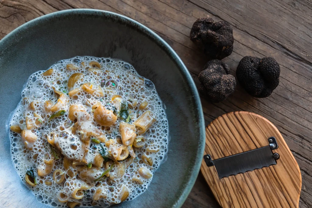 Overhead view of pasta with black truffles and a shaver on wood.