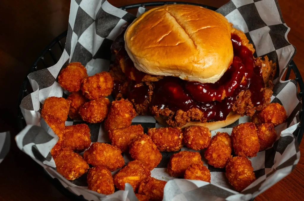 Barbecue fried chicken sandwich and tater tots in checkered basket.