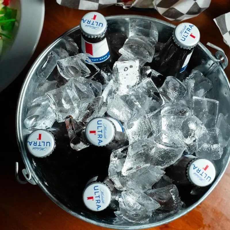 Top-down of galvanized bucket with Michelob Ultra bottles, ice, and food.