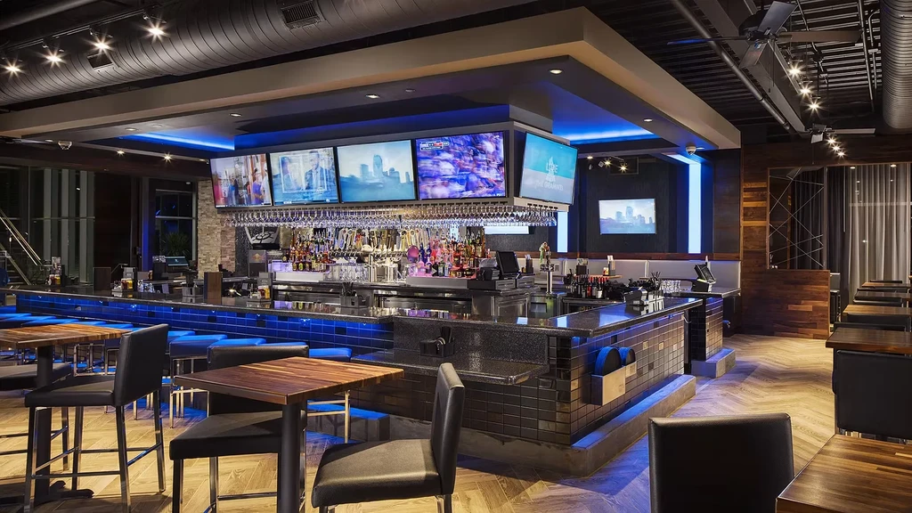 Well-lit, fully stocked bar with blue LED strip and multiple TVs.