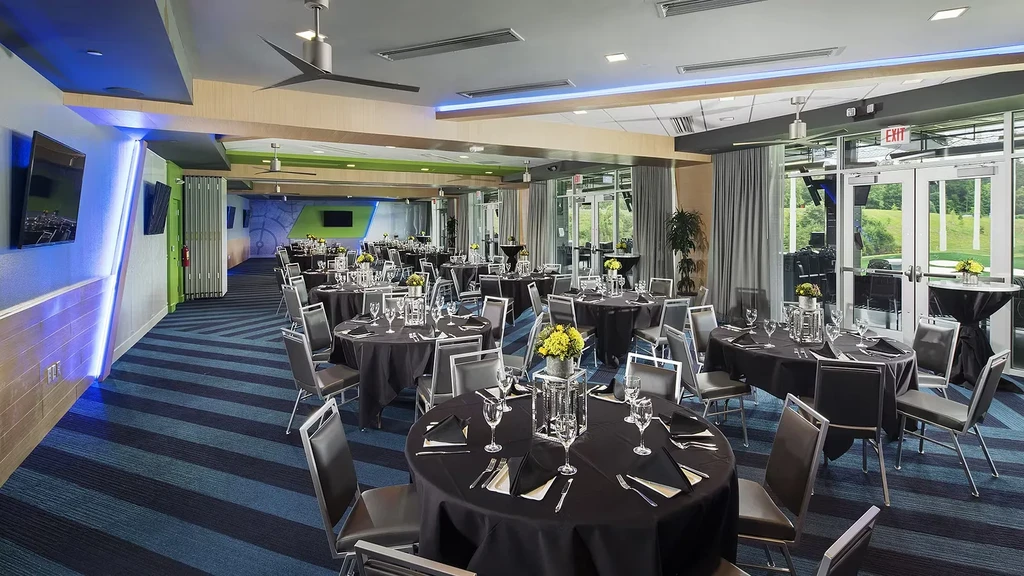 Modern banquet hall with many tables, yellow floral centerpieces, outdoor view.