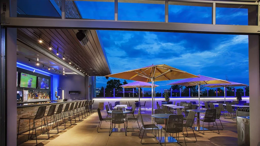 Modern open-air bar and patio at twilight, with warm and blue lights.