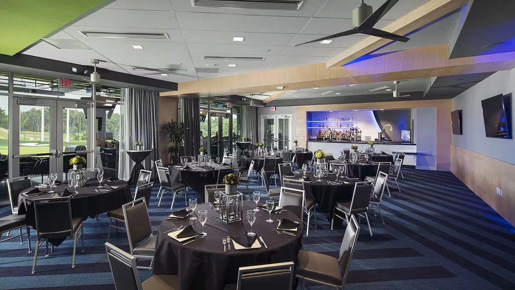 Empty modern banquet hall, golf course view, black tables, blue-lit bar.