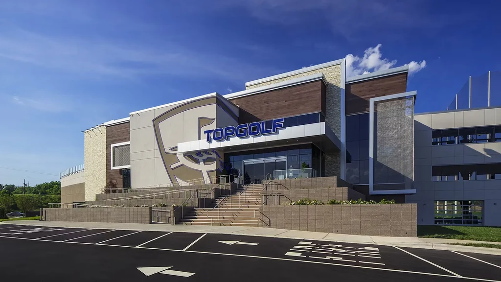 Large, modern TOPGOLF building exterior with parking lot and blue sky.