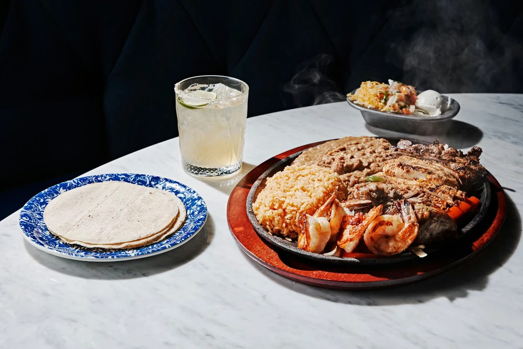 Sizzling fajitas with chicken, beef, shrimp, rice, beans, and tortillas.
