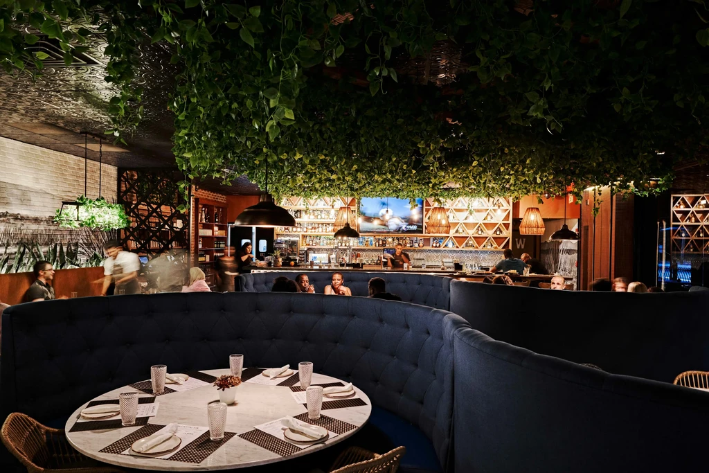 Botanical restaurant interior with green foliage ceiling, navy banquettes, and bar.