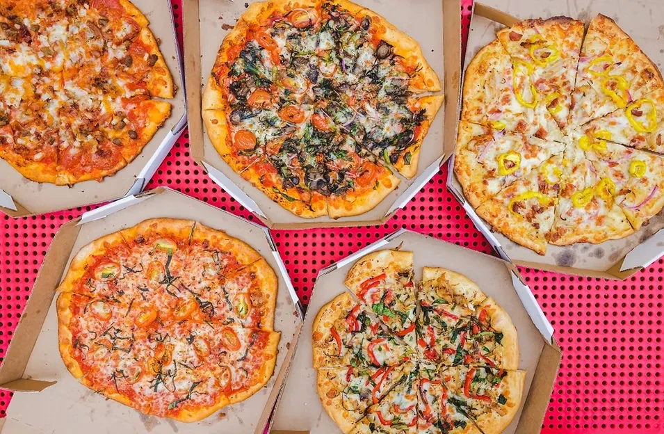 Overhead shot of five diverse pizzas in open boxes on red.