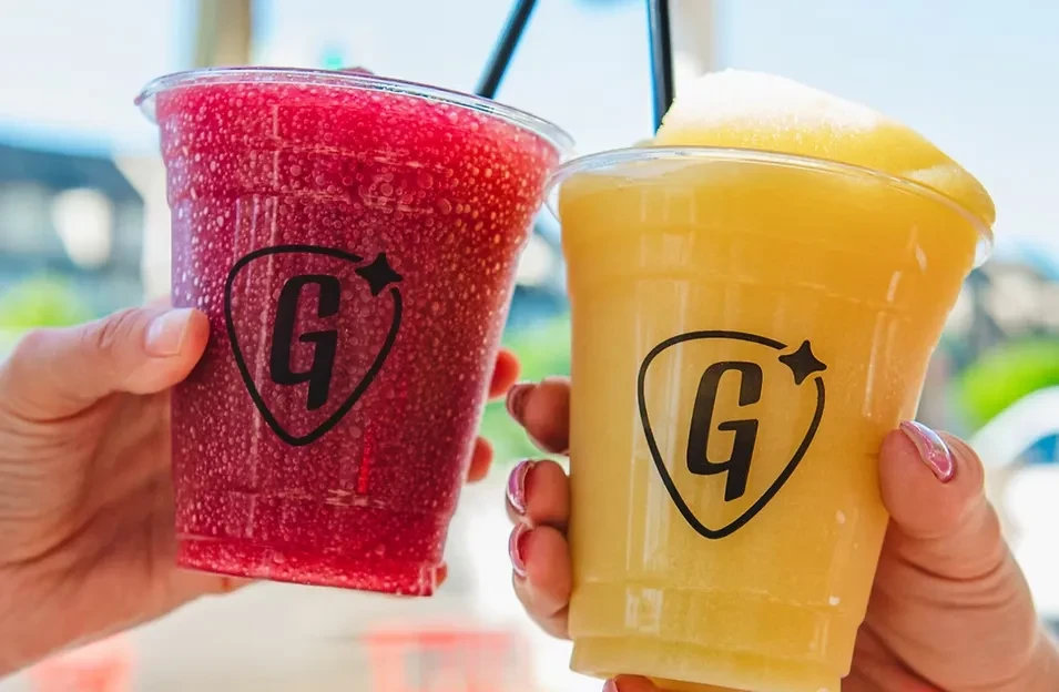 Close-up of two hands holding G-logo cups with colorful slushies.