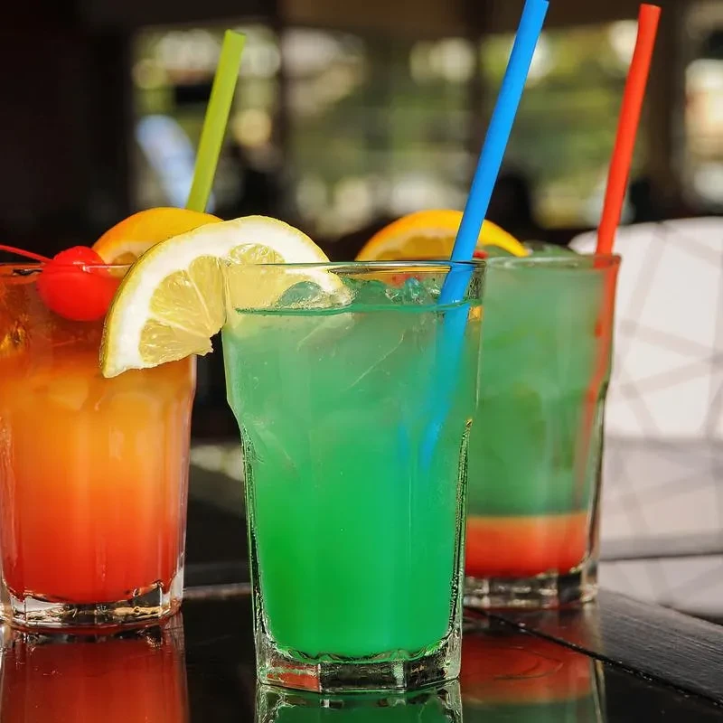 Three vibrant cocktails with fruit garnishes on a reflective surface.