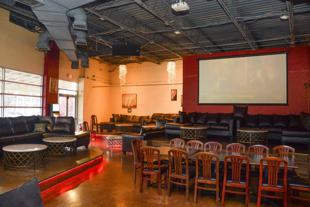 Modern industrial-chic lounge with dark leather seating, dining tables, projector screen.