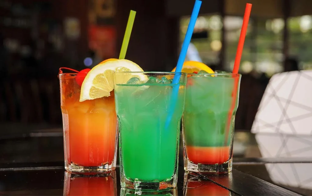 Three vibrant, colorful cocktails with garnishes on a reflective surface.