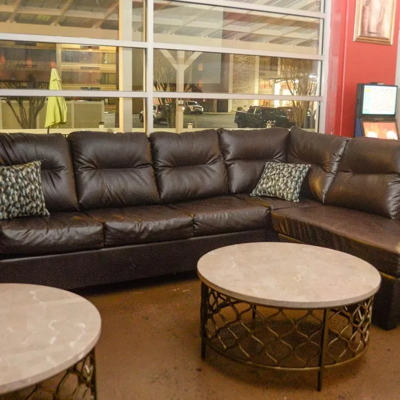 Dark brown leather sectional sofa, coffee tables, large windows, and night view.
