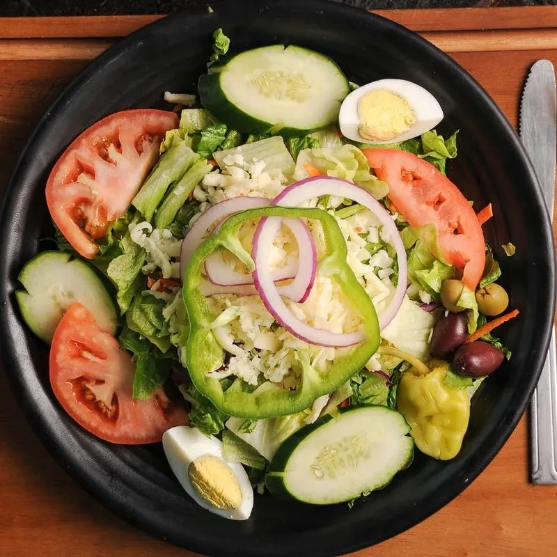 Garden salad with egg, olives, and cheese in a black bowl.