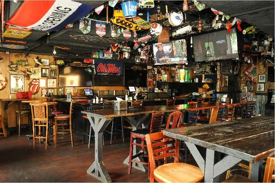 Decorated casual bar interior with memorabilia, signs, TVs, and dark furniture.