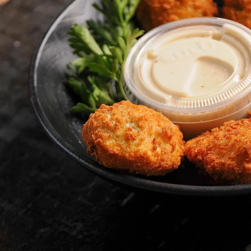 Close-up of golden-brown fried nuggets with parsley and dipping sauce.