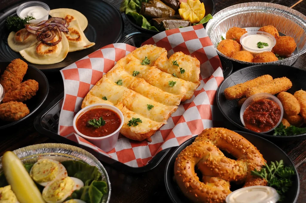 Table full of appetizers: cheese breadsticks, pierogi, fried chicken, pretzel.