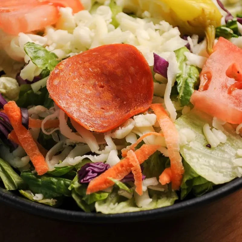 Close-up of fresh salad with lettuce, cheese, pepperoni, tomato, carrots.