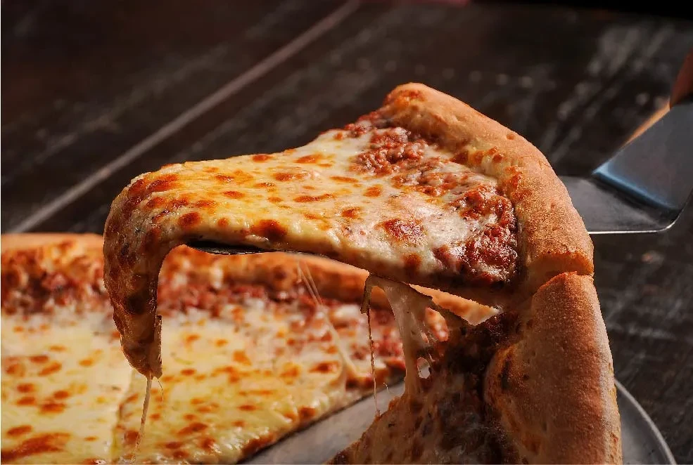 Pizza slice lifted, melted cheese stretching and dripping.