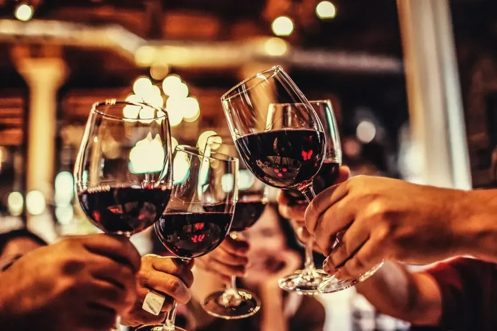 Close-up of multiple hands holding red wine glasses in a toast.