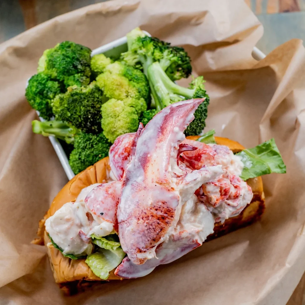 Close-up of a lobster roll with a claw, served with roasted broccoli.