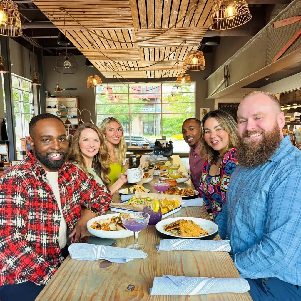 Six smiling people enjoy tacos and drinks at a modern restaurant.