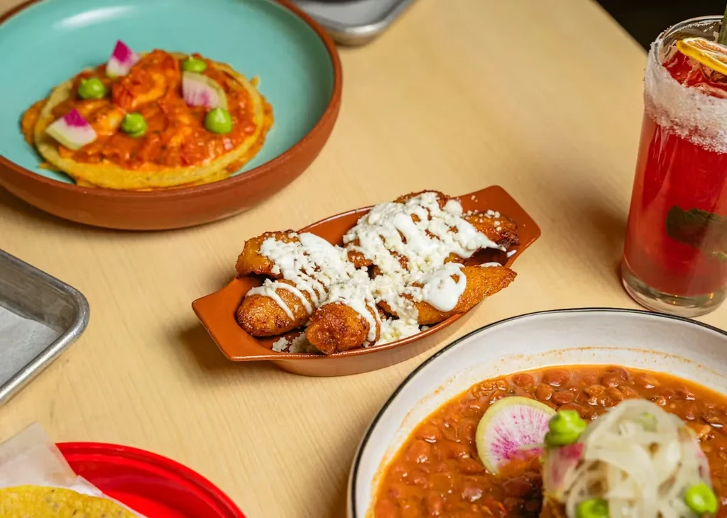 Colorful spread of shrimp dish, plantains, bean stew, and red drink.