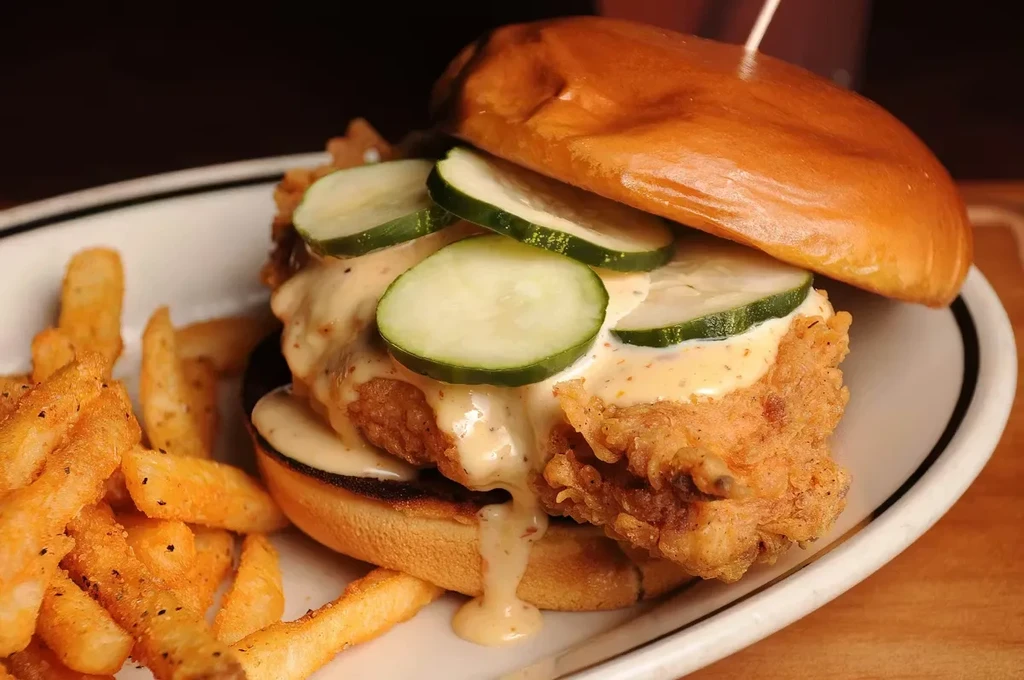 Crispy fried chicken sandwich with pickles, sauce, and fries.