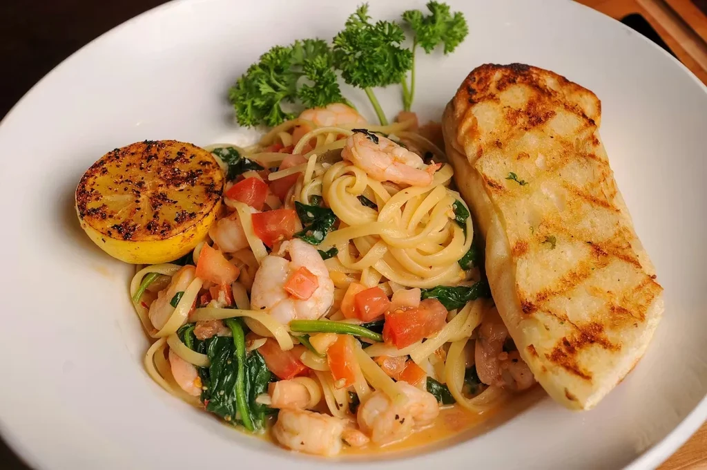 Shrimp pasta with tomatoes, spinach, grilled lemon, and grilled bread.