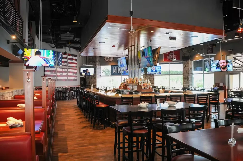 Empty modern sports bar with large bar, red booths, and many TVs.